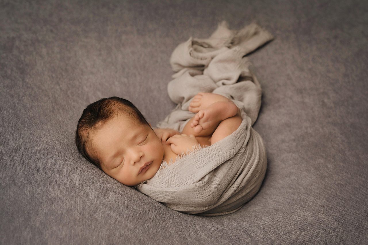newborn baby swaddled in warm grey knitted blanket on soft pillow