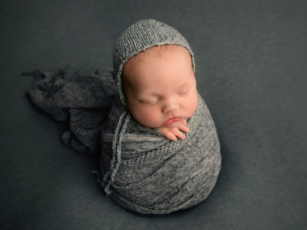 small newborn swaddled in a blue-grey, knitted blanket