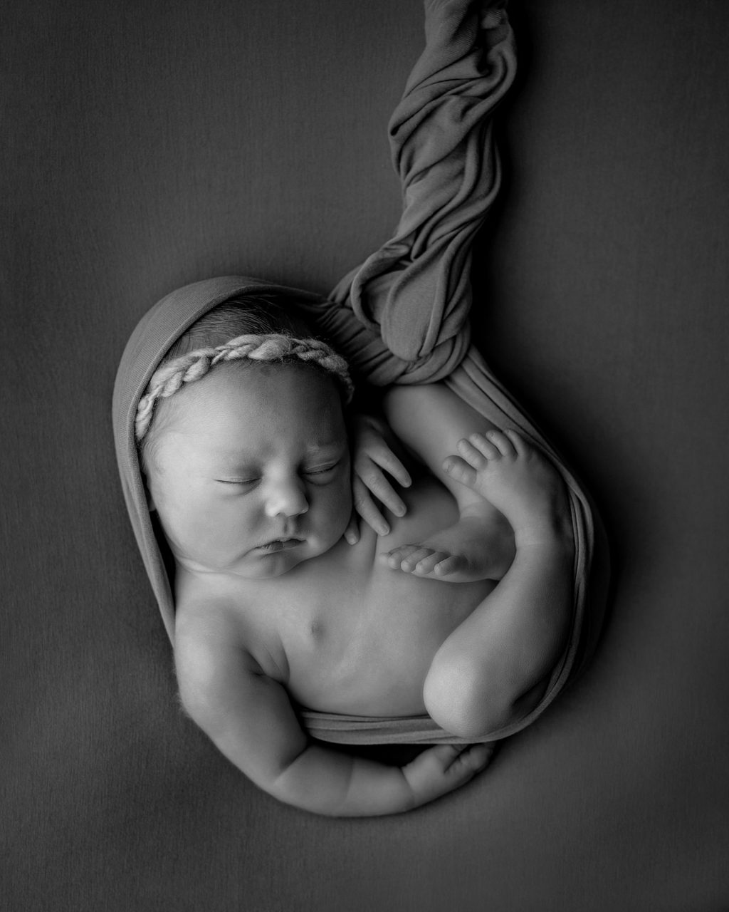 newborn baby on soft pillow posed like they're in the womb, with a knitted blanket as the umbilical chord 