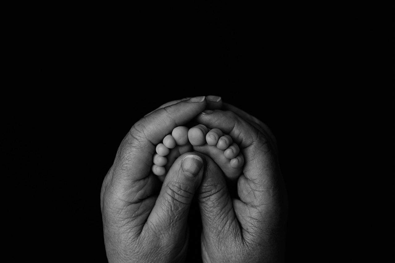 black and white image of a small baby's feet embraced by the hands of an older woman