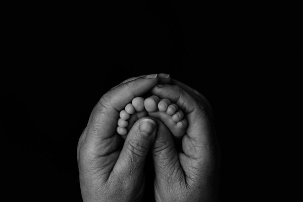 black and white image of a small baby's feet embraced by the hands of an older woman