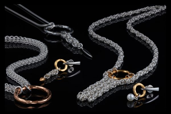 silver chainmail jewelry with golden rings on a black, reflective surface
