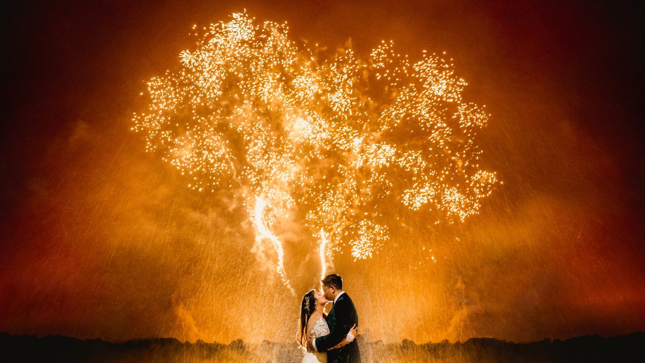 bride and groom kissing in front of amber fireworks
