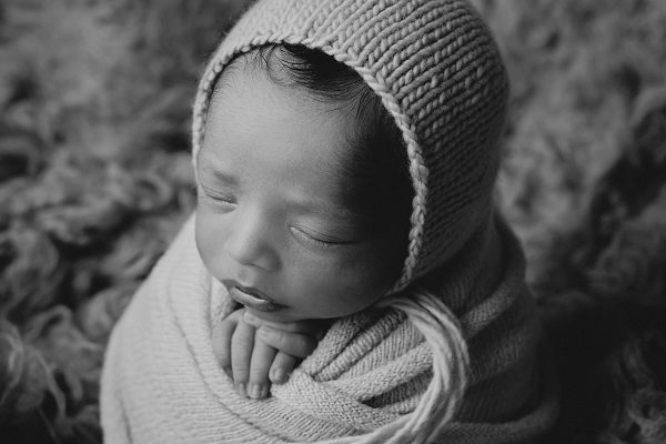 black and white photo of a newborn baby, wrapped in wool blanket and in a potato stack pose