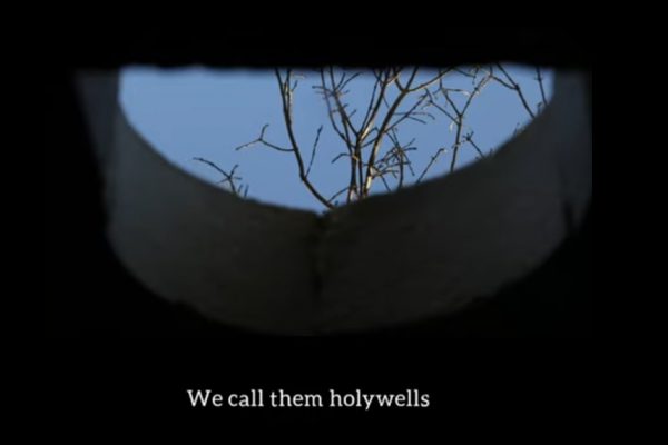 still image from a video of a reflection in a well of a bare tree. There are subtitles at the bottom that say "we call then Holy Wells"